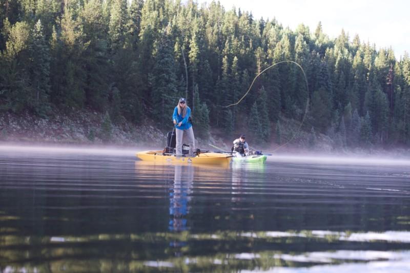 Angler on kayak casts into a misty mountain lake