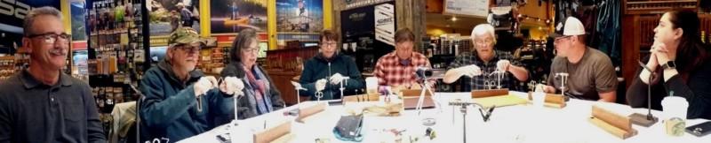Fly tying students sit in a row, practicing tying